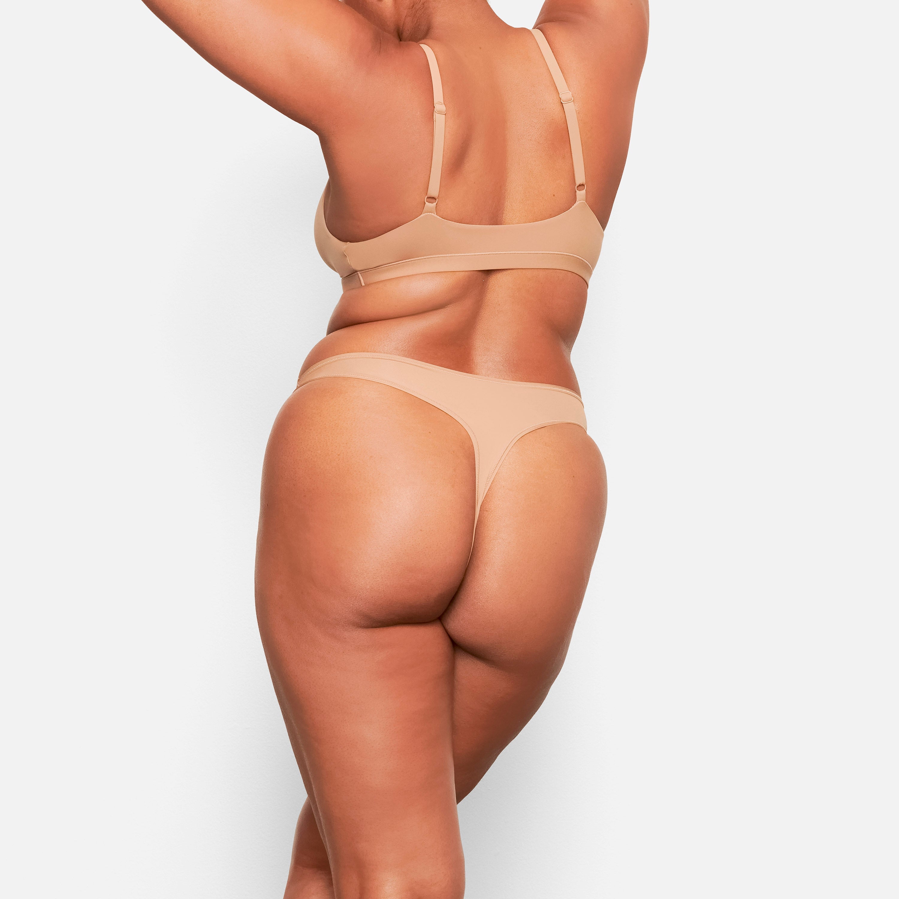 A MODEL STANDS FACING FORWARD WEARING THE SKIMS FITS EVERYBODY TRIANGLE BRALETTE IN SIENNA |