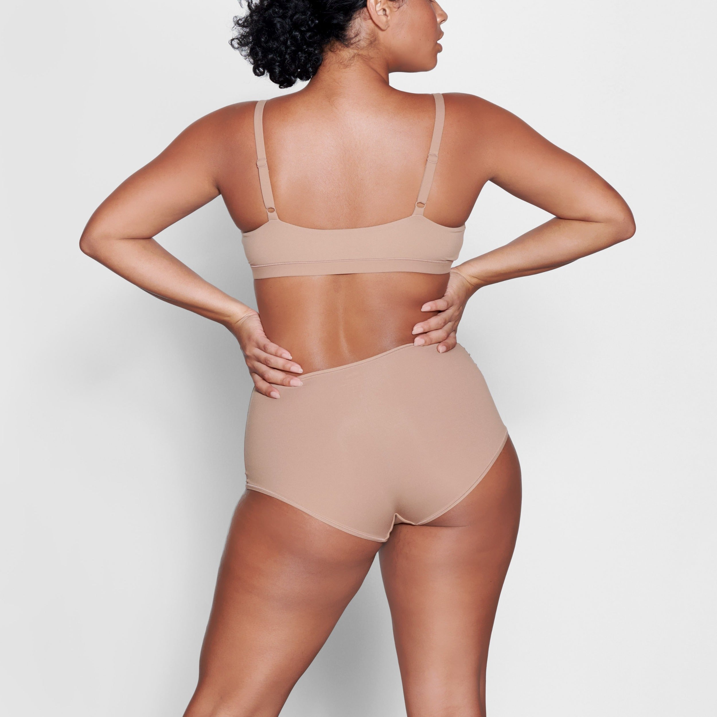 A MODEL STANDS WITH HER BACK TO THE CAMERA SHOWING THE FITS EVERYBODY BOY SHORT | SIENNA