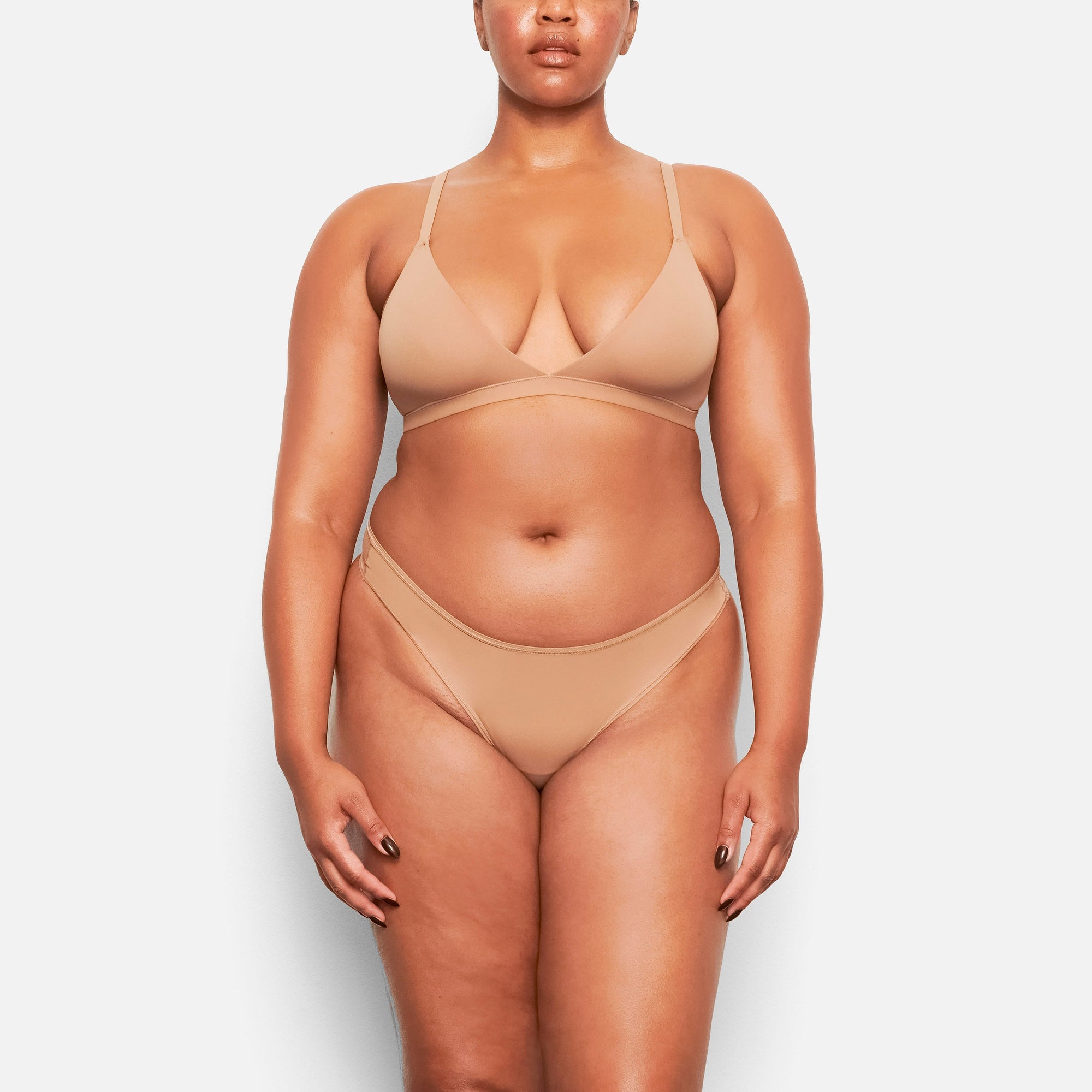 A MODEL STANDS FACING FORWARD WEARING THE SKIMS FITS EVERYBODY TRIANGLE BRALETTE IN SIENNA | SEE: M, L, XL