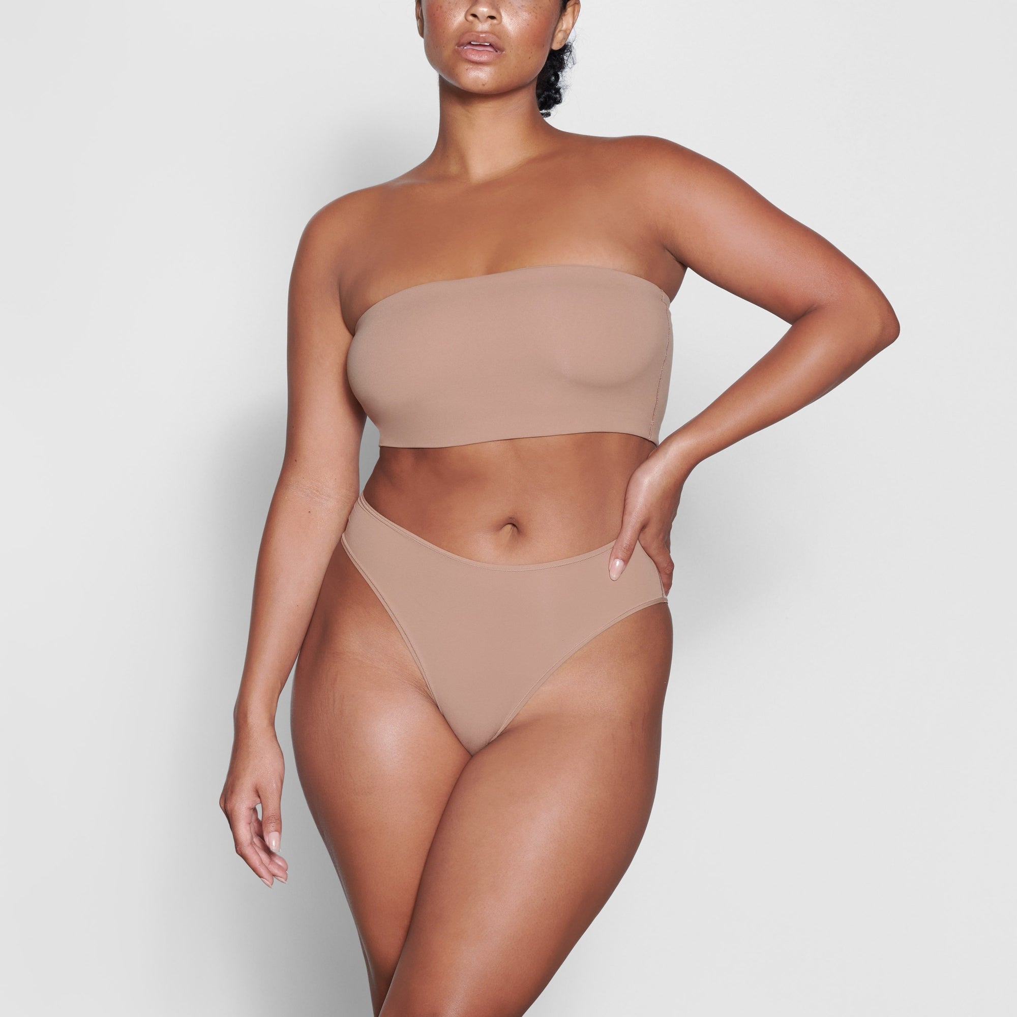 A MODEL STANDS FACING FORWARD WEARING THE SKIMS FITS EVERYBODY CHEEKY BRIEF IN SIENNA | SEE: M, L