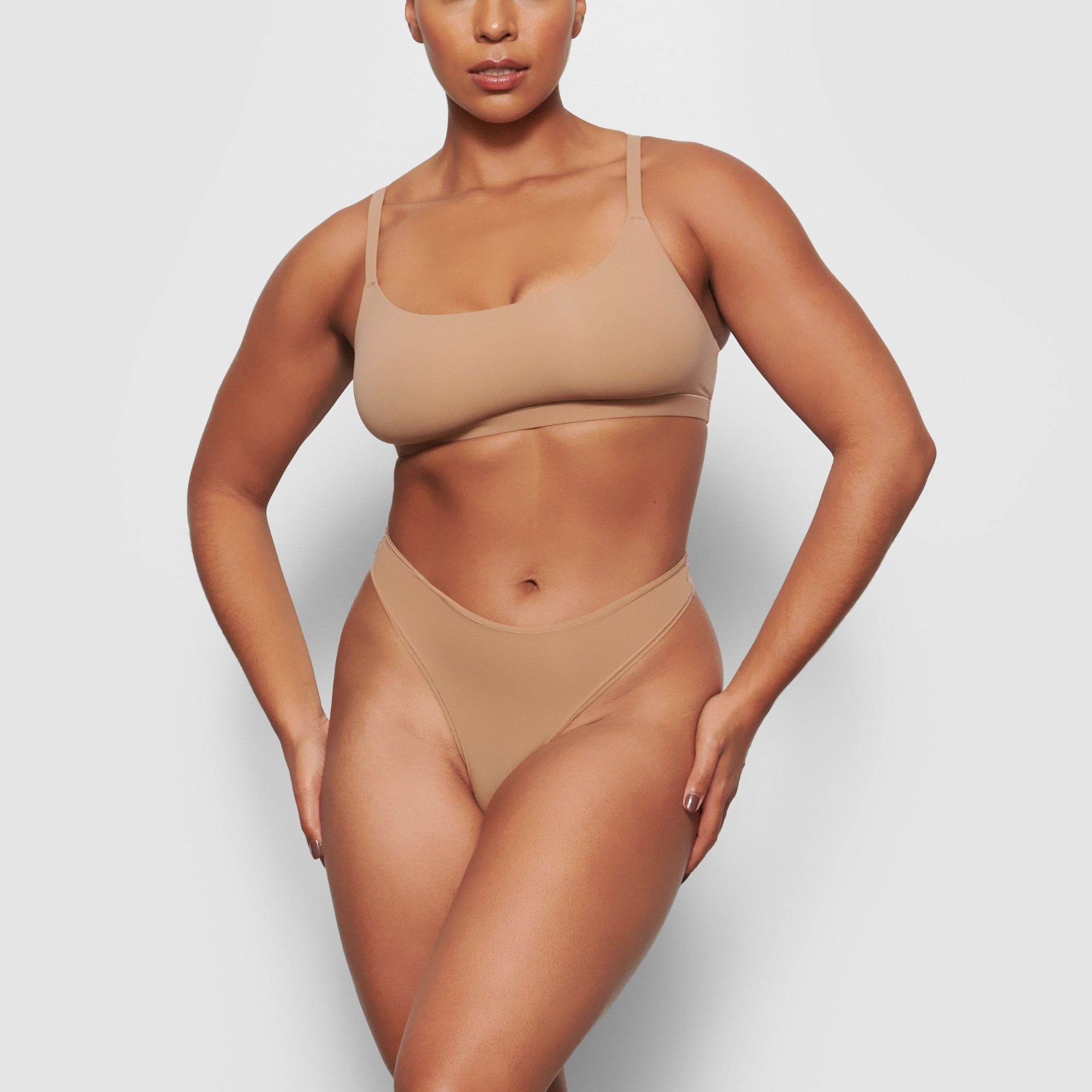 A MODEL STANDS FACING FORWARD WEARING THE SKIMS FITS EVERYBODY THONG IN SIENNA | SEE: M, L, XL